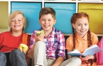 Drei Schulkinder sitzen auf dem Boden und essen Äpfel